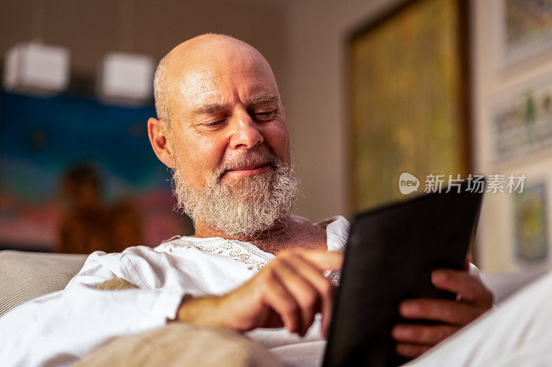 一位自信而快乐的老人在他舒适的客厅里用平板电脑咨询他的投资。