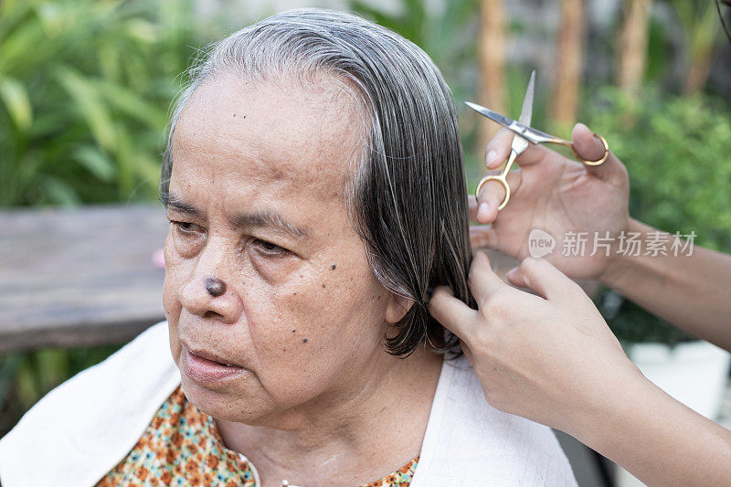 有爱心的女人看护者，在家里剪她年迈的女人头发