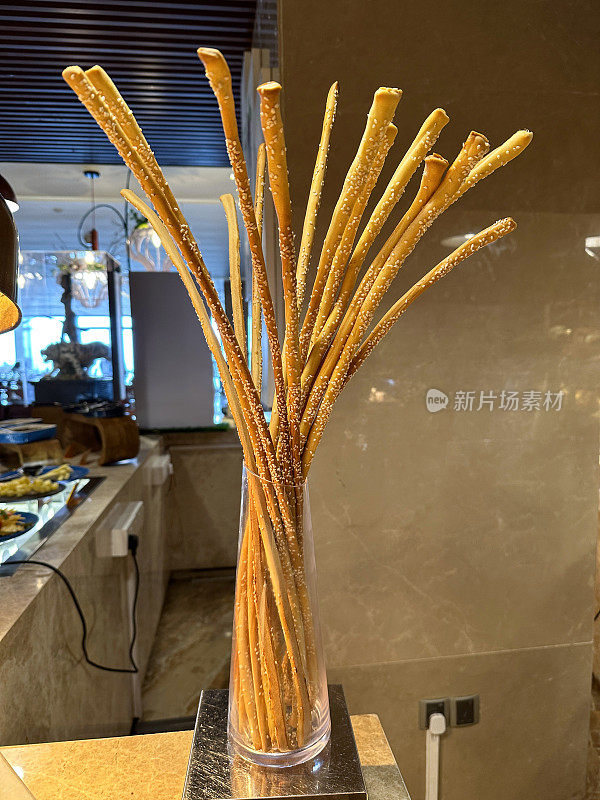 餐厅自助面包店货架上手工面包棒堆叠在玻璃花瓶中的图像，重点在前景