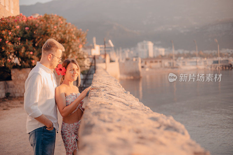一对年轻夫妇站在海边的一堵墙旁，看着什么东西
