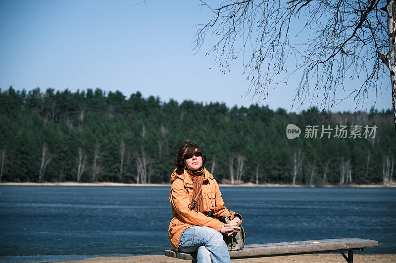 一个女人坐在森林湖岸的长椅上，享受着阳光