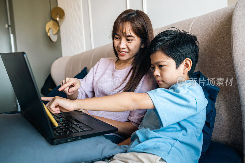 一位亚洲母亲和她的儿子一起在家里玩笔记本电脑。