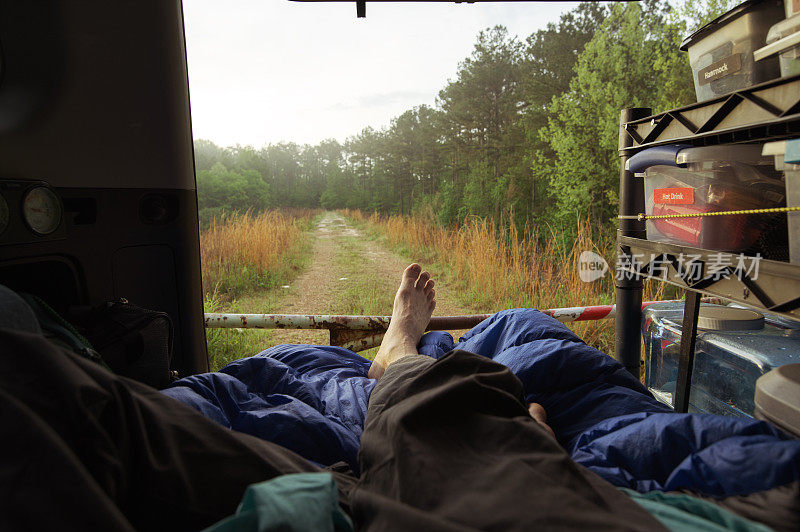 无法辨认的人躺在床垫上，而露营在陆路车辆的后面