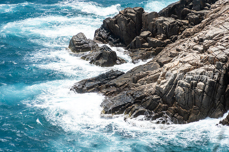 海浪拍打着海滩上的岩石，海水随着阳光飞溅到天空。一个宁静的越南孔岛，是越南海岛的天堂