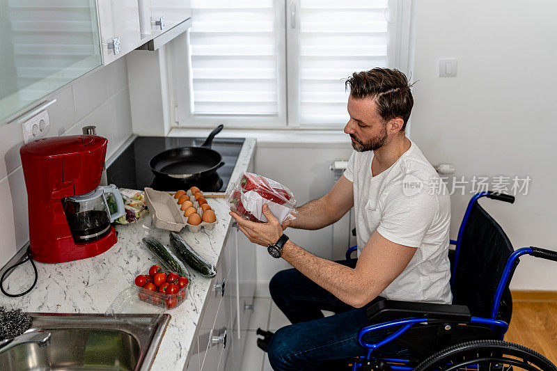 坚定而独立。坐在轮椅上的中年男子在他的无障碍厨房里准备饭菜