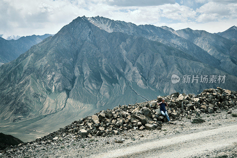 一位女背包客坐在高山路旁的岩石上休息