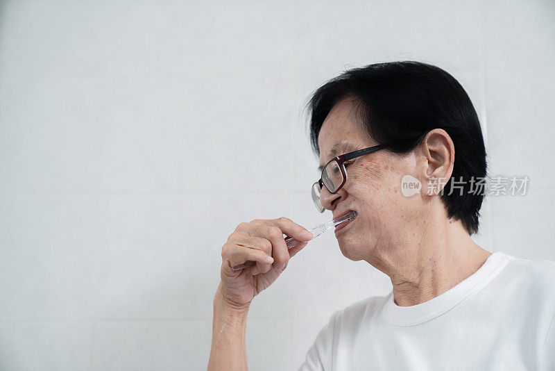 亚洲老年妇女在家庭浴室照顾口腔卫生。