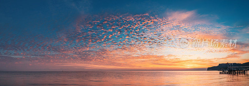 海边的神奇时刻，当太阳的第一缕光线穿透云层，在宁静的水面上创造出万花筒般的色彩