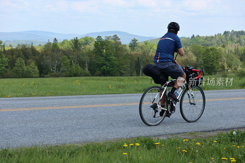 一个人骑着自行车在乡村公路上，背景是山(没有脸，看向别处，砾石自行车设置与自行车背包)旅行，旅游，骑自行车，骑自行车，自行车