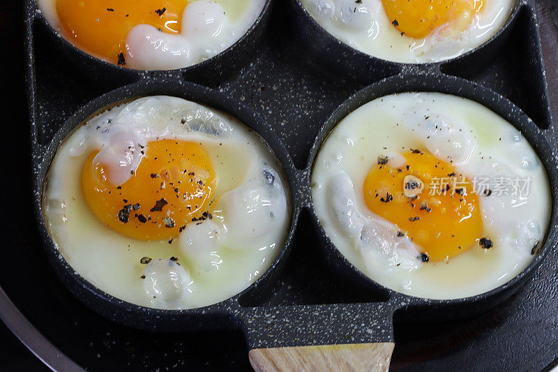 特写图片:带有煎蛋环的不粘锅，四个鸡蛋在陶瓷滚刀上的煎锅里煮