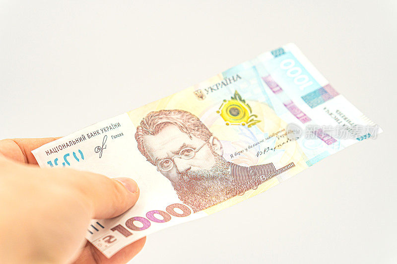 乌克兰现金货币的概念。现金支付在乌克兰。一个人用乌克兰的钱付钱。手里拿着1000格里夫纳，孤立在白底上。乌克兰最大面值的钞票