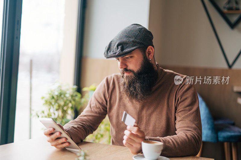 一个年轻人在咖啡馆喝咖啡，用数码平板电脑在网上购物