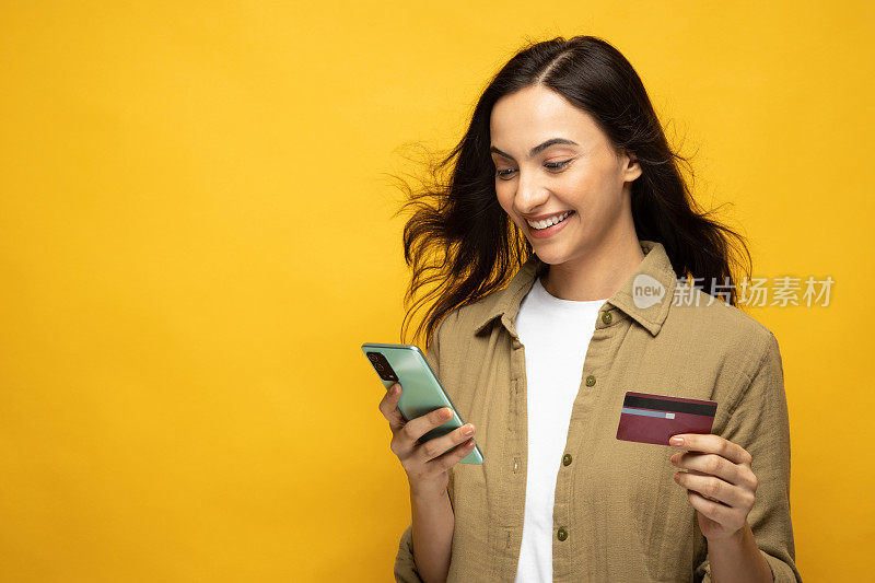 有吸引力的开朗女孩的肖像使用设备应用程序银行卡预订孤立在黄色背景股票照片