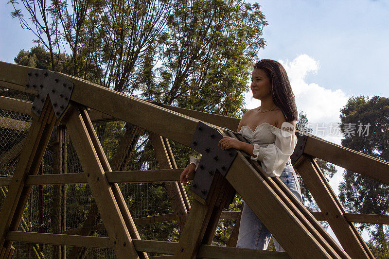 美丽的年轻女子站在公园的木桥上，望向别处
