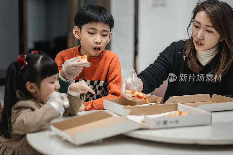 一位亚洲母亲和她的孩子正在家里吃外卖披萨