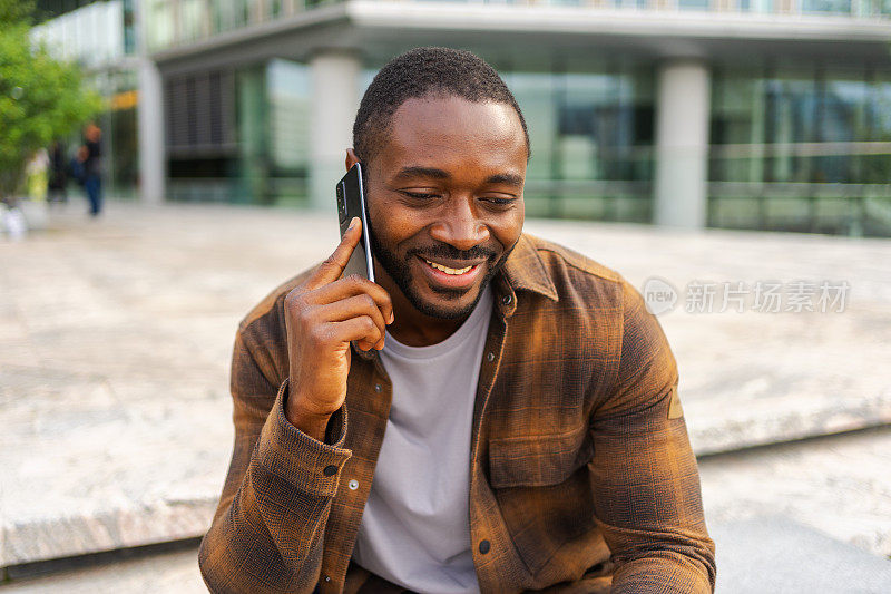 非裔美国人在城市户外的街道上讲智能手机。拿着手机和朋友聊天的男人。微笑的人用手机接电话。有人在用手机聊天。