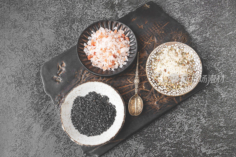 不同种类的盐-喜马拉雅粉，黑，和五香盐在一个手工牛皮盘子上的粘土砧板。俯视图