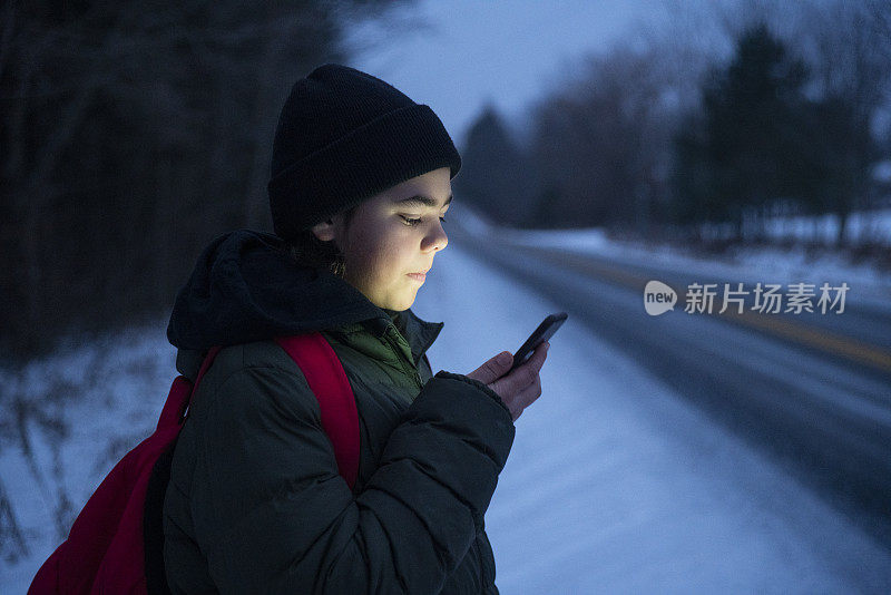 一名青少年在冬天等校车的时候用智能手机和朋友在社交媒体上联系