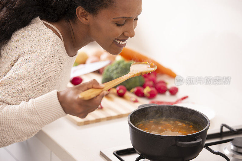 女人在厨房里用木勺品尝汤。