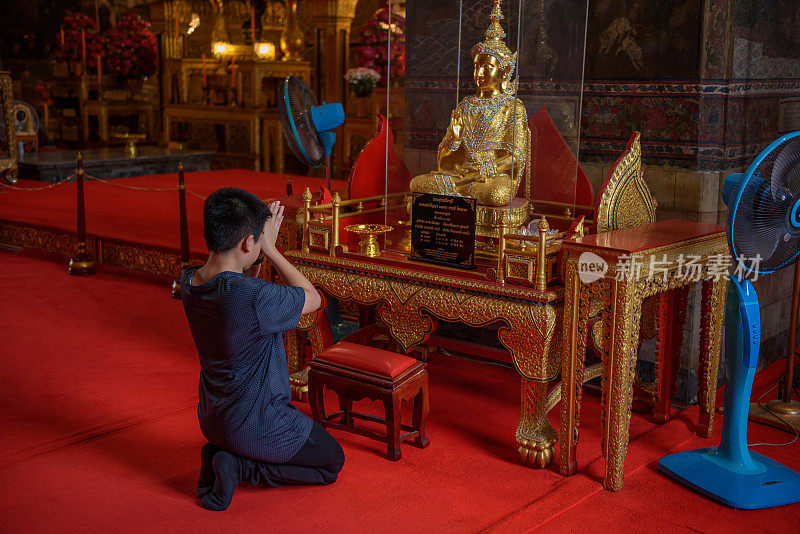 年轻的亚洲男孩在苏特寺向佛祈祷