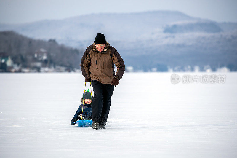 冬天，爷爷在冰湖上拉着孙子的雪橇