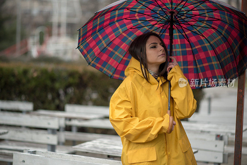 穿着黄色雨衣的年轻女子在公园里度过雨天