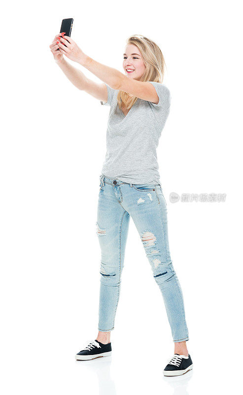 z一代的年轻女性穿着牛仔裤站在白色背景前用手机拍照