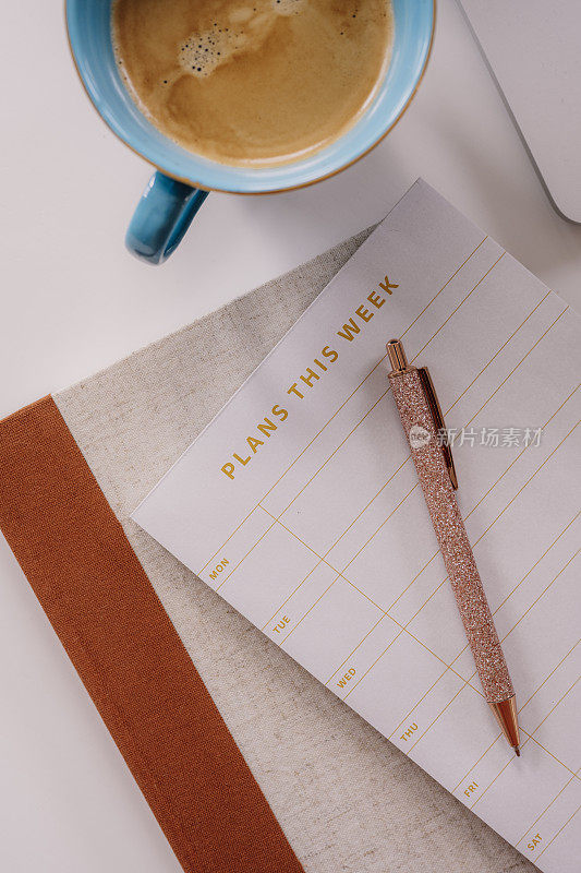 每周计划者的静物生活在家里的桌子上，拿着咖啡和笔