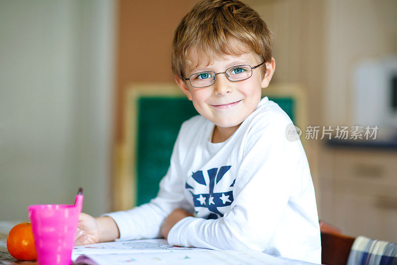 快乐的小学生戴着眼镜在家里做作业