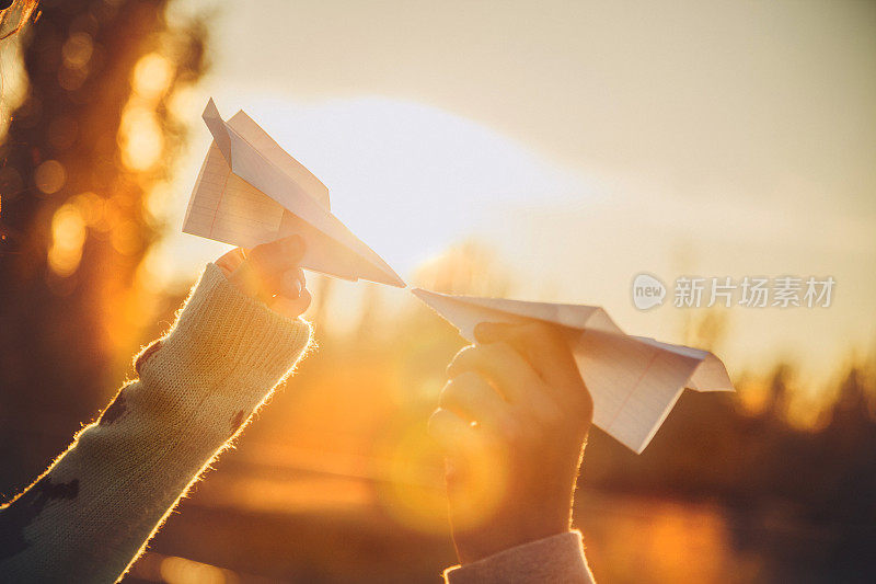 两架纸飞机在日落的时候手拿着看着对方