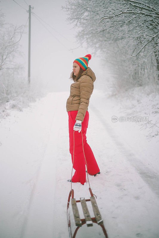 女孩在森林里散步，拉雪橇。一个开心的女人。圣诞假期。女孩免费休息。圣诞树躺在雪橇上。美丽的年轻女孩或女人在森林里散步。拉木制雪橇