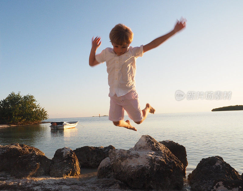 日落时分，小男孩在海滩边的空中跳跃