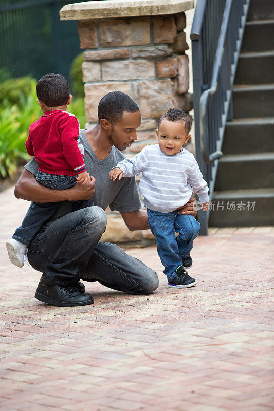 一位非裔美国父亲带着一对双胞胎儿子跪在人行道上