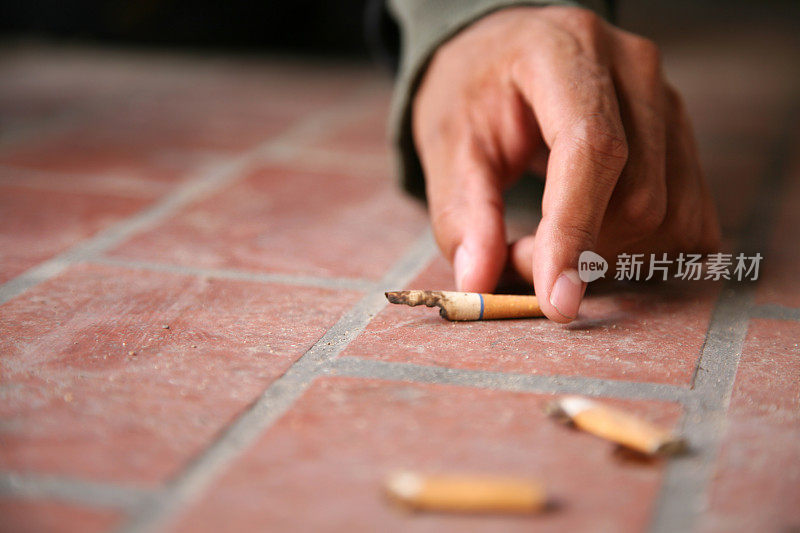 一个男人从肮脏的地上捡起一支二手烟