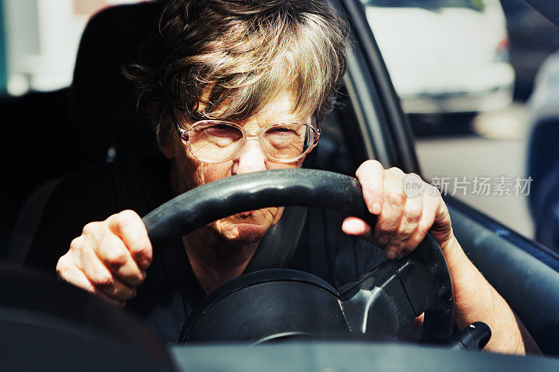 老妇人在车流中开车时，紧皱着眉头，全神贯注