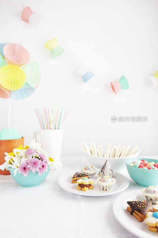 派对桌上放着雏菊，纸杯蛋糕内衬修剪植物和花环