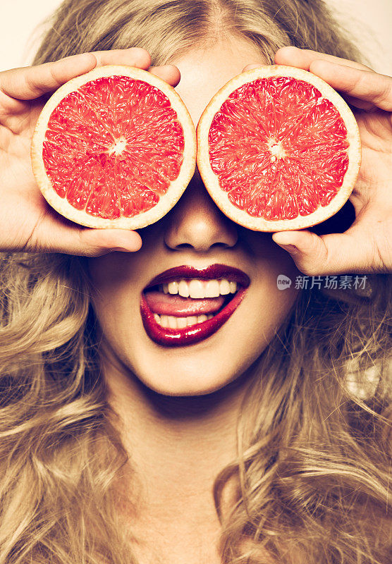 滑稽的肖像女孩拿着红葡萄柚在她的脸前面