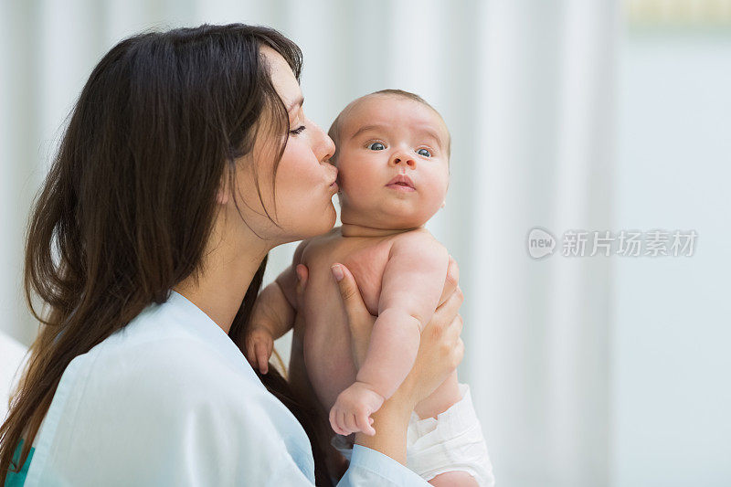 妈妈亲吻一个穿着尿布的婴儿