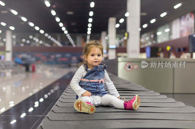 可爱的小女孩坐在机场的皮带上