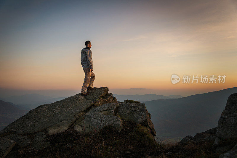 日落时分，一个人站在山顶的岩石上