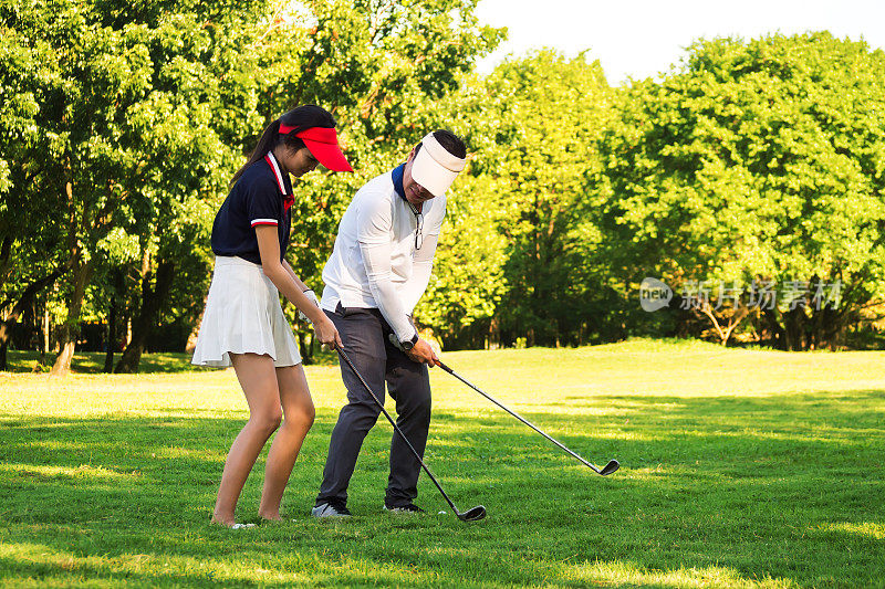 亚洲高尔夫教练教年轻女子打高尔夫球。在实践中公园。商务人士最喜欢的运动。