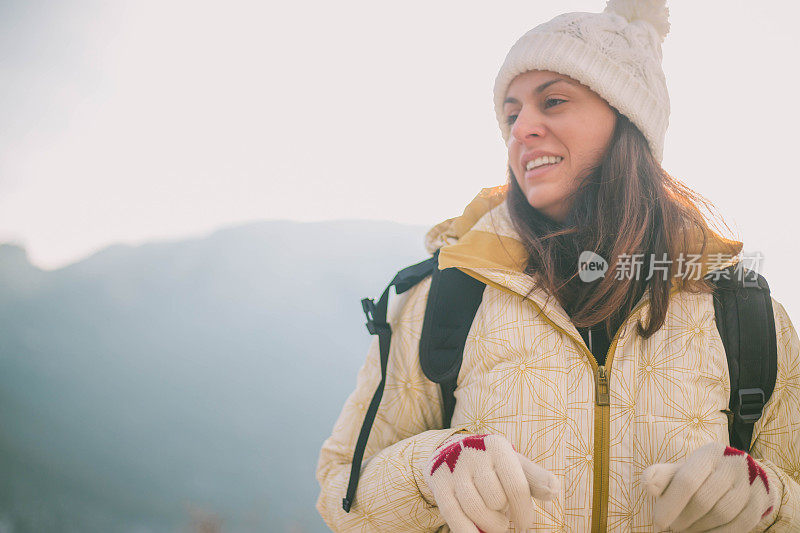 近景美丽的年轻女子在冬天的衣服站在一边，手拿木棍的背景雪山