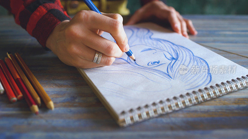 特写的女性手绘素描在纸笔记本与铅笔。工作中的女艺术家