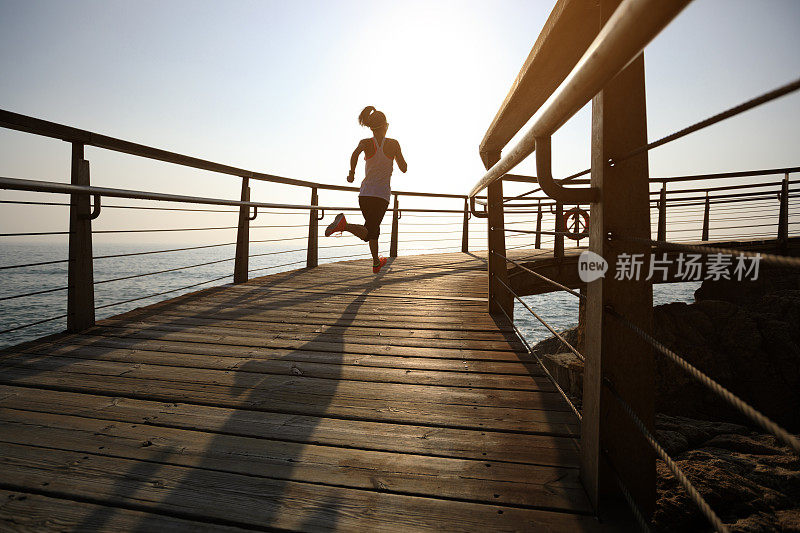 运动健身女性跑步在海滨木板路在日出