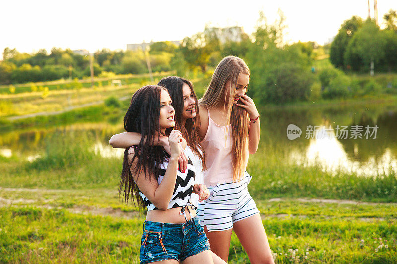 三个美丽的女孩在公园的夕阳下散步和欢笑。友谊的概念。