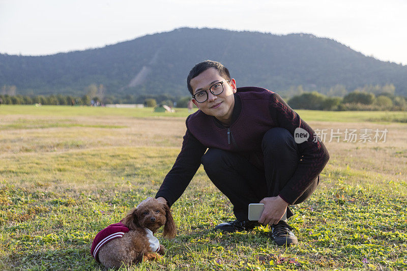 男主人坐在草坪上和狮子狗玩耍