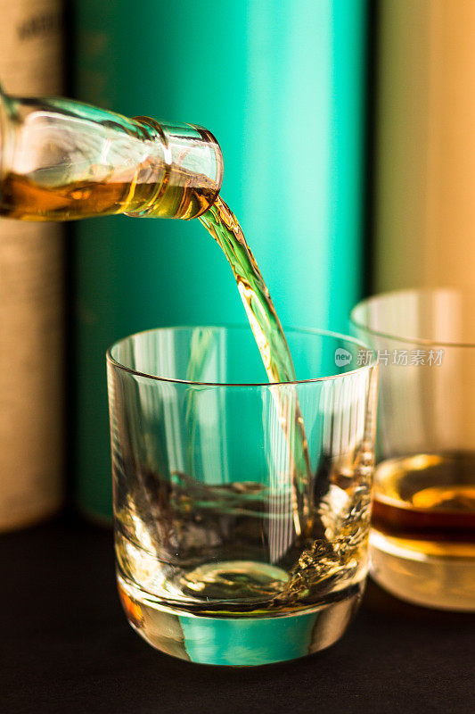 威士忌从透明玻璃瓶倒入玻璃杯，背景是苏格兰麦芽威士忌瓶