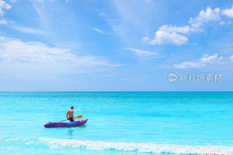 一个男人拉着皮划艇在蔚蓝的大海上度假度假，夏日时光概念
