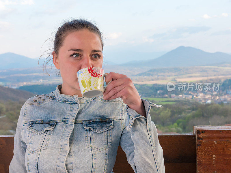 特写的年轻女子站在阳台上喝咖啡或茶美丽的风景在背景