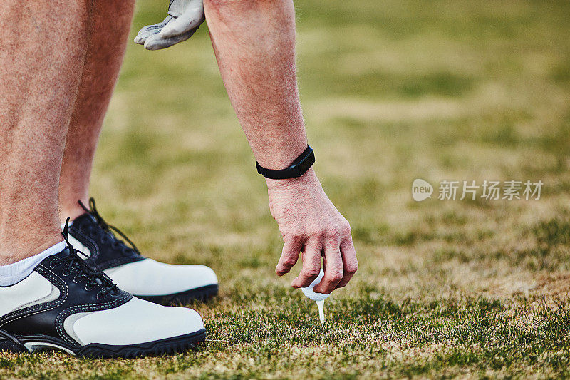 男性高尔夫球手佩戴健身追踪器将高尔夫球放在球座上